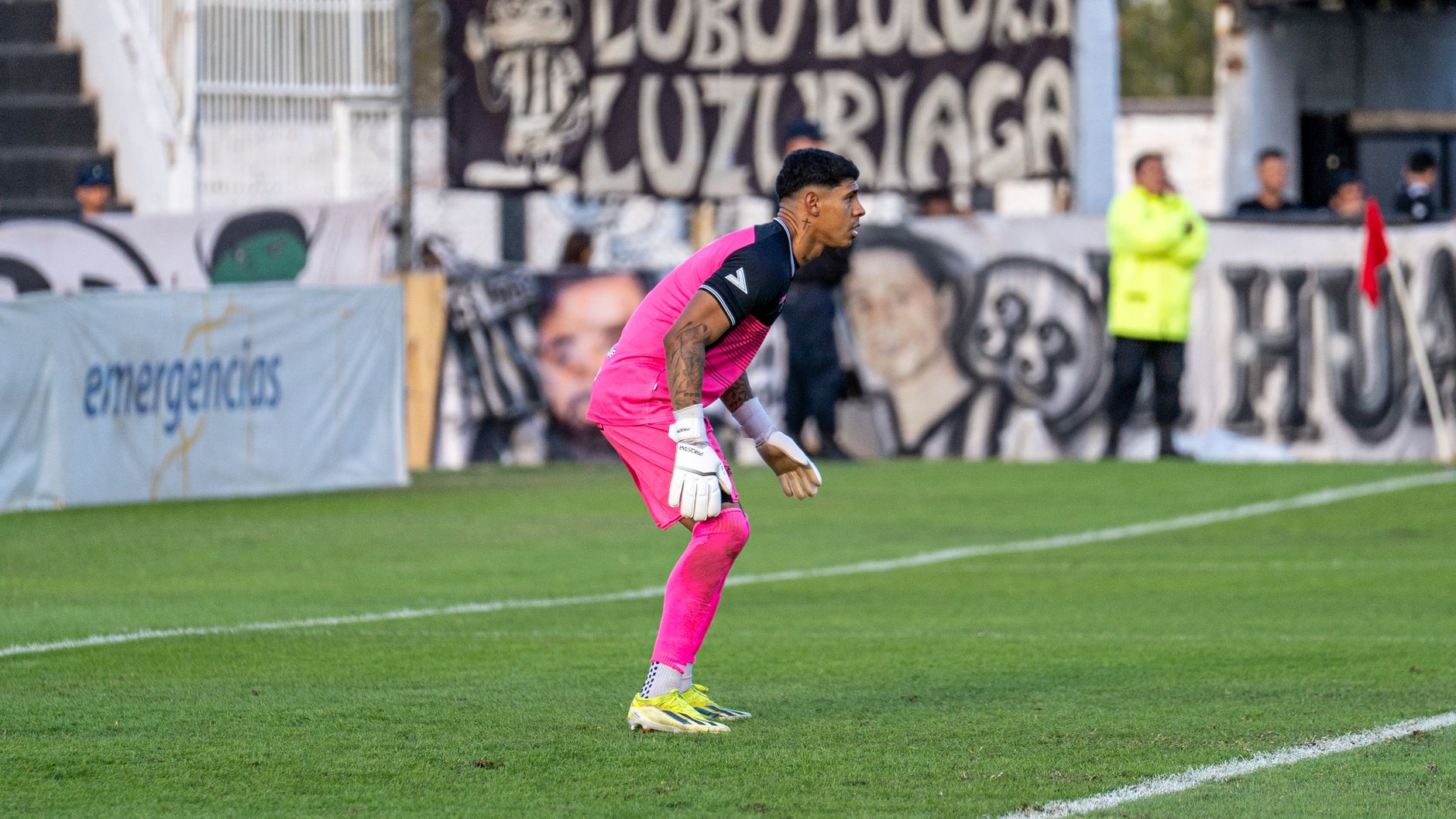 Soccer goalkeeper in vibrant pink uniform poised during a match on a bright day.