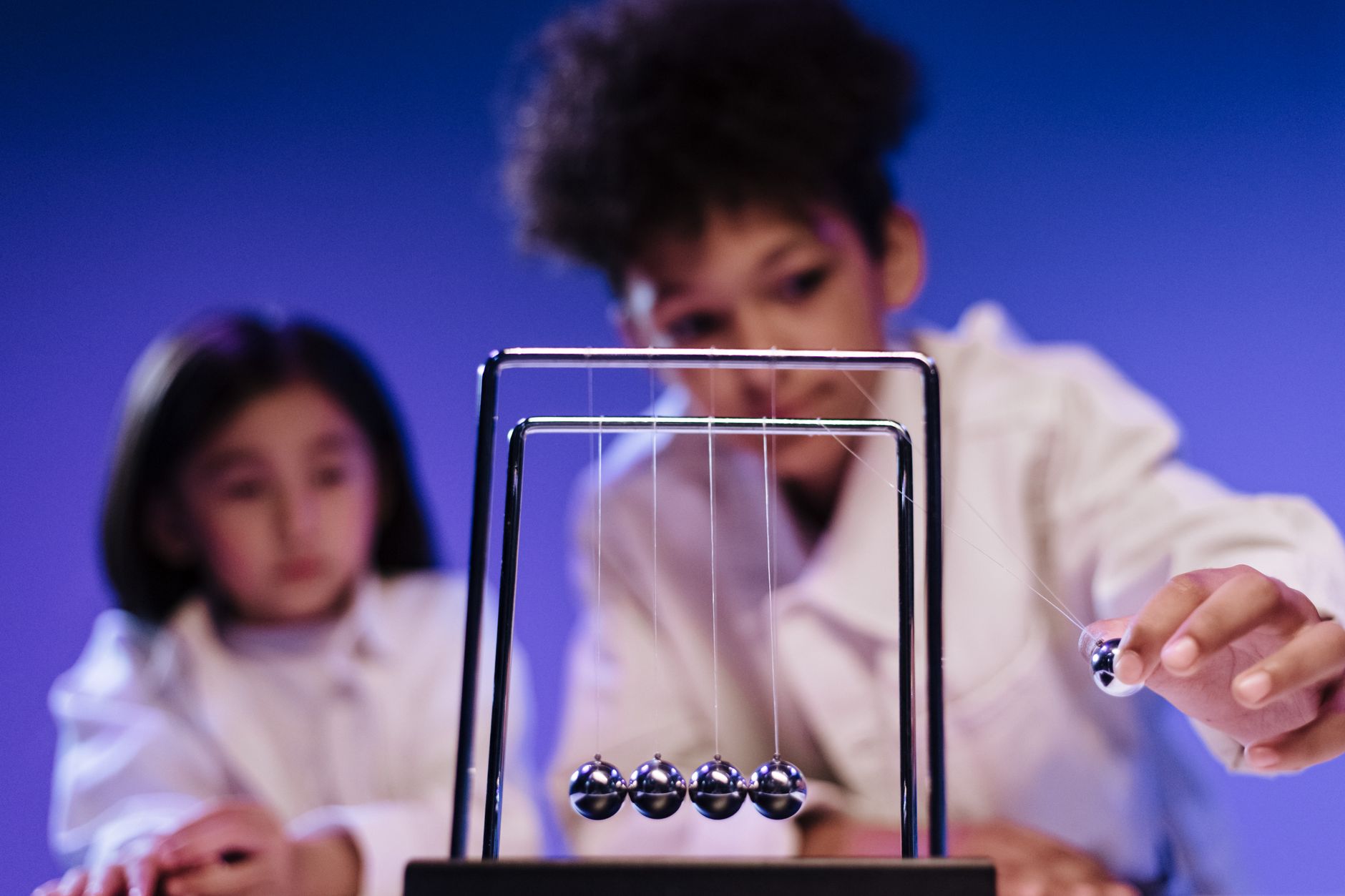 A boy and a girl engaged with a Newton's Cradle in a science setting, showcasing curiosity and learning.