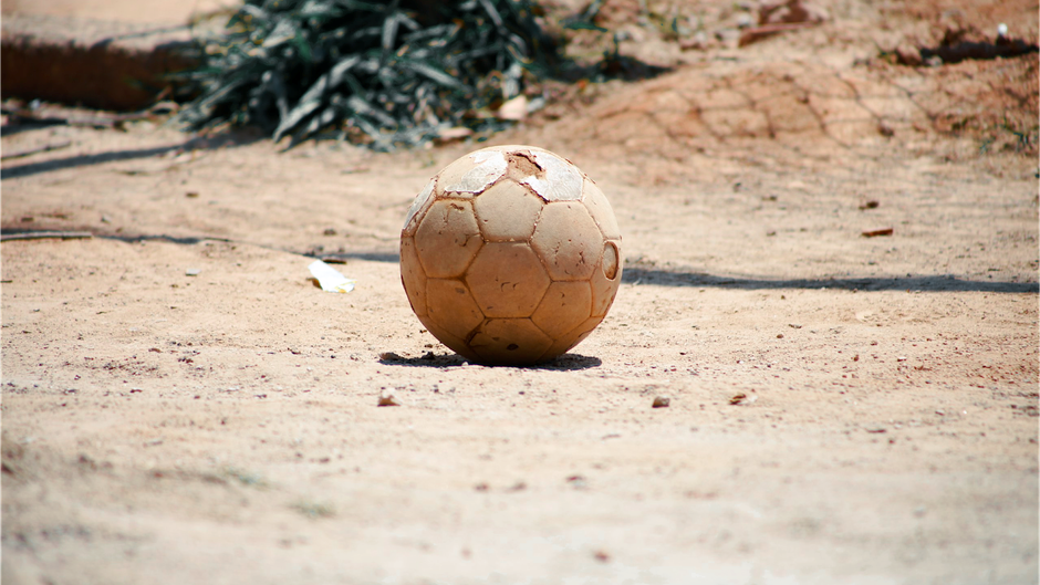 A worn soccer ball resting on a dusty outdoor field, embodying a vintage playground feel.