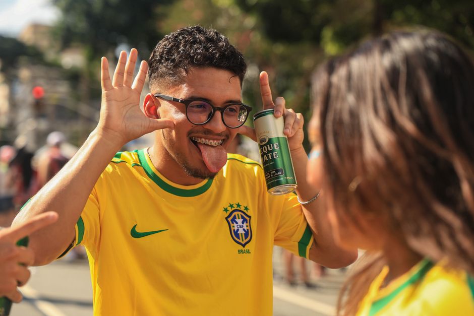 Happy Brazilian football fan in yellow jersey making playful gestures during a lively outdoor event.