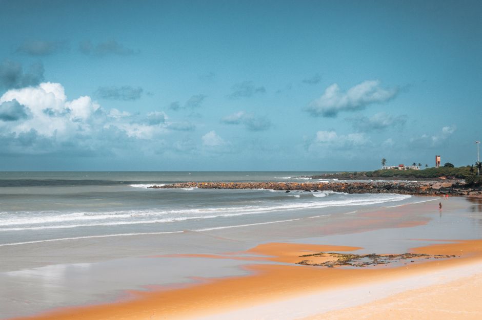 Tranquil view of a scenic beach in Natal, Brazil showing waves and a distant lighthouse.