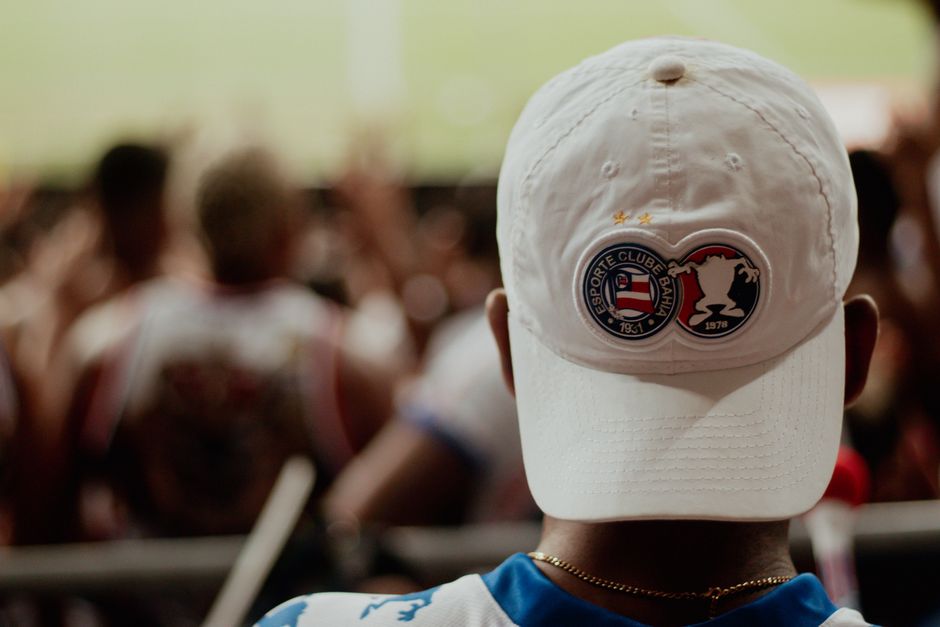 A dedicated football fan sport ing an Esporte Clube Bahia cap watches the game.