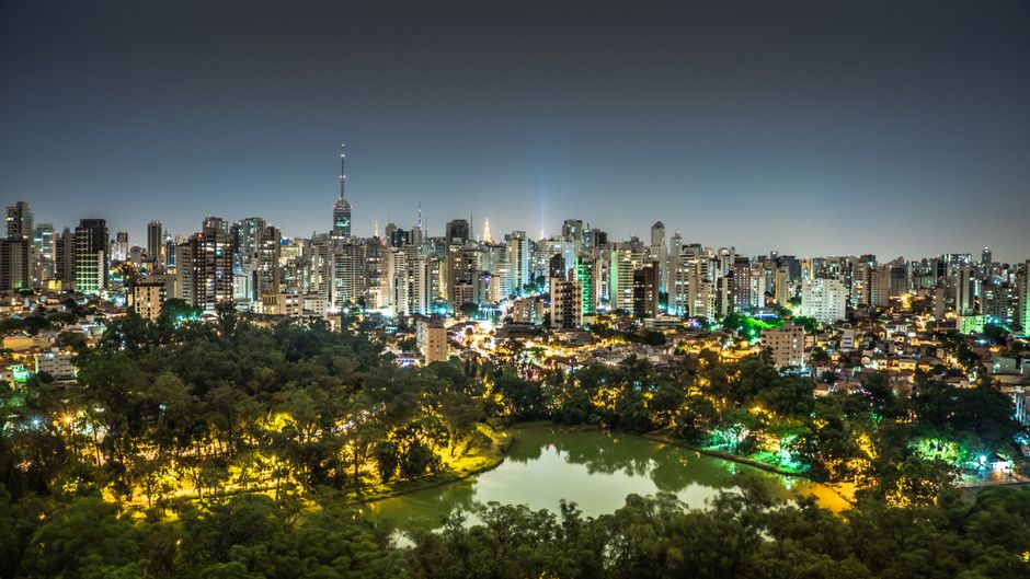Night view of São Paulo's illuminated skyline with a park and lake in the foreground.