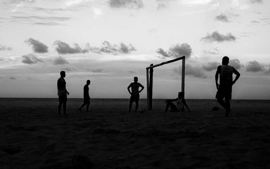 Silhouetted group playing soccer on a beach at sunset in Natal, Brazil.