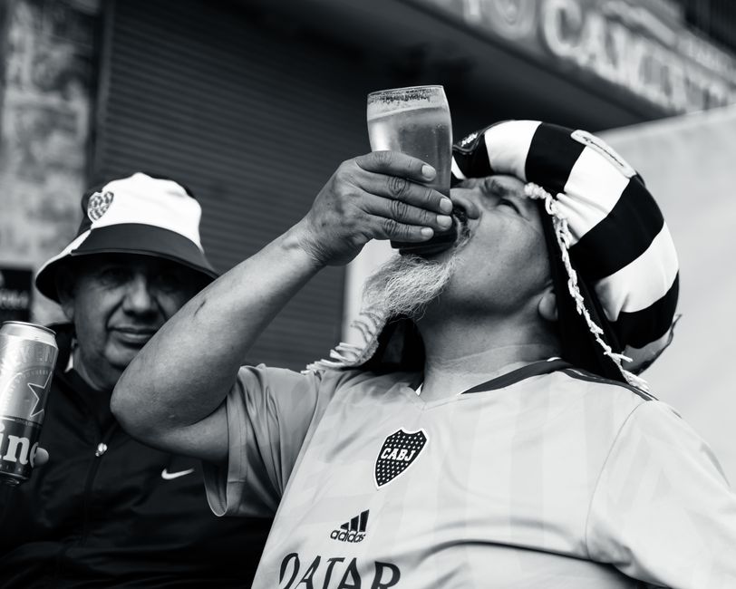 A passionate football fan in a striped hat enjoying a beer on a sunny day with friends.
