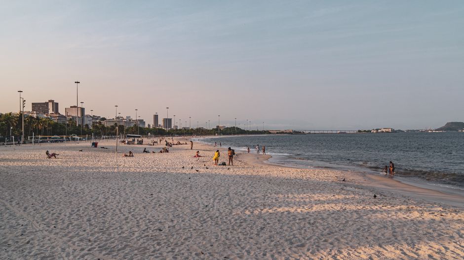 People enjoying a sunny day on Flamengo Beach in Rio de Janeiro, with city skyline views.