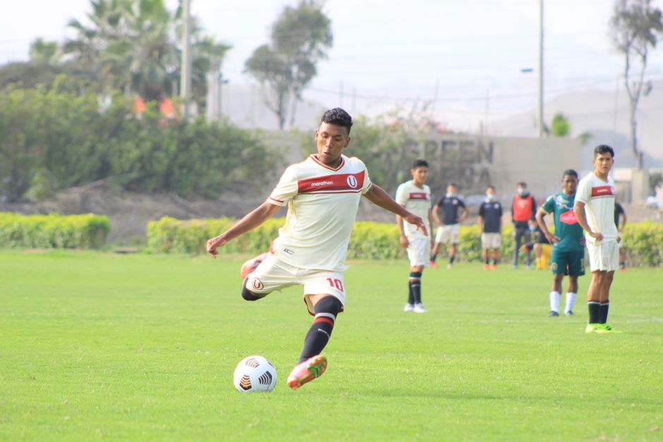 A soccer player kicks a ball on a lush green field during a sunny day in Lurín, Perú.