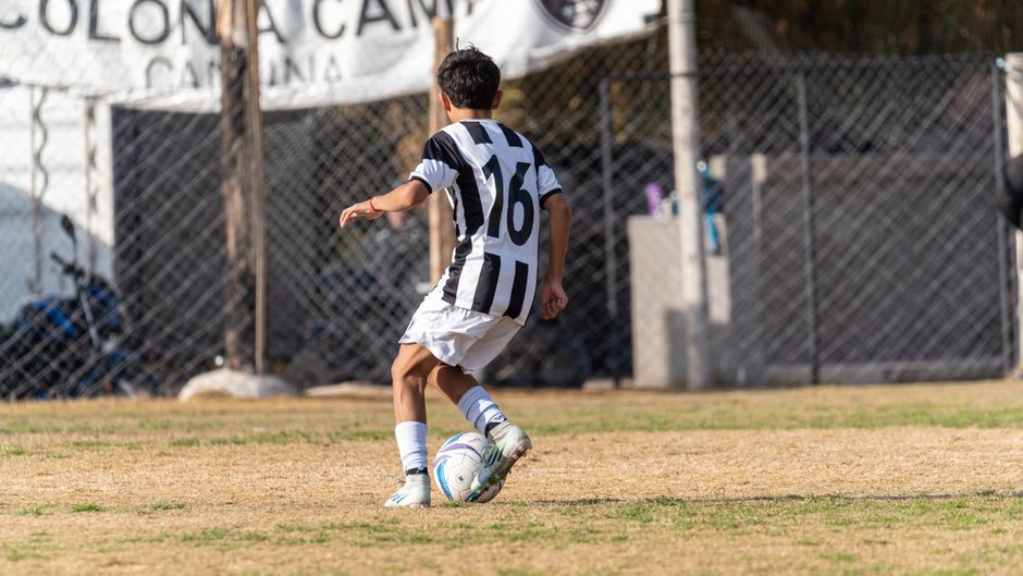 A young soccer player wearing a striped jersey dribbles the ball on an outdoor field during a game.