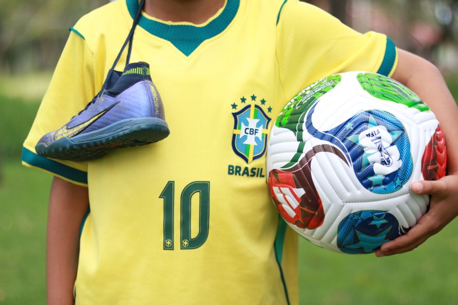 Youth wearing Brazilian jersey with soccer ball and shoes, ready to play outdoors.