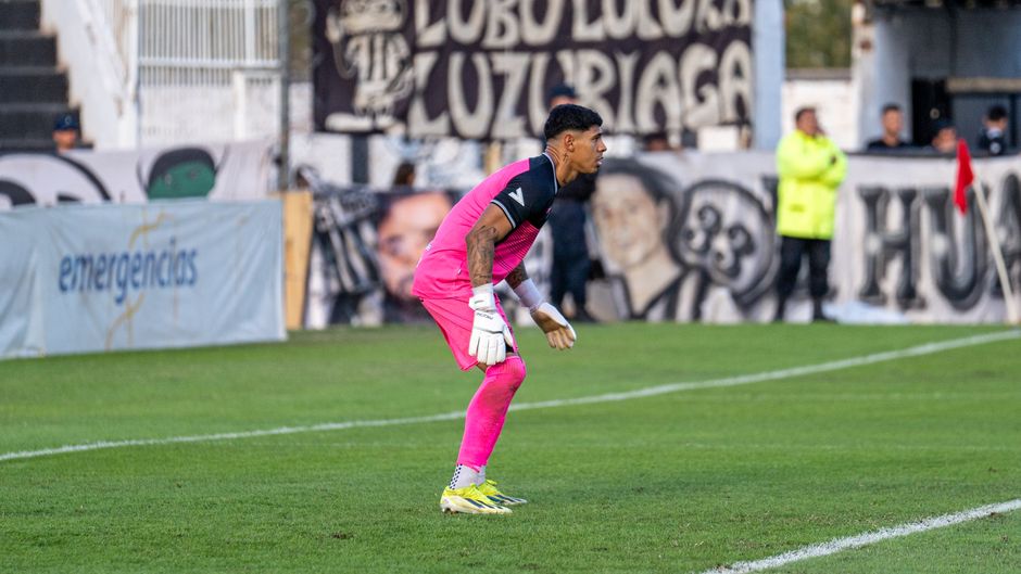 Soccer goalkeeper in vibrant pink uniform poised during a match on a bright day.