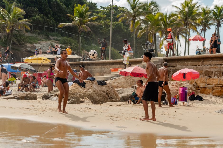 Diverse group engaging in beach soccer under palm trees, creating a lively summer atmosphere.
