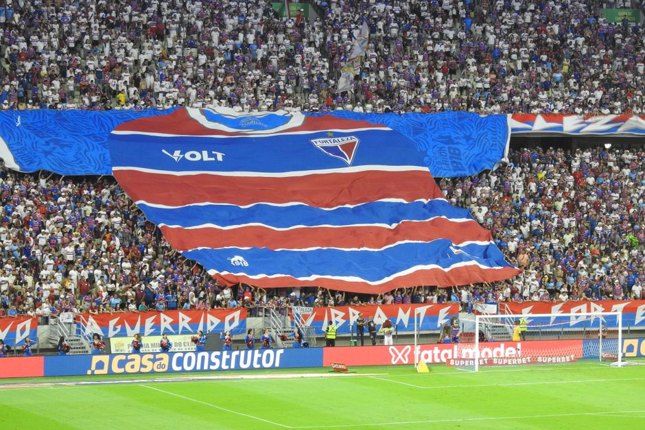 Large Fortaleza shirt banner held by fans in a bustling stadium.