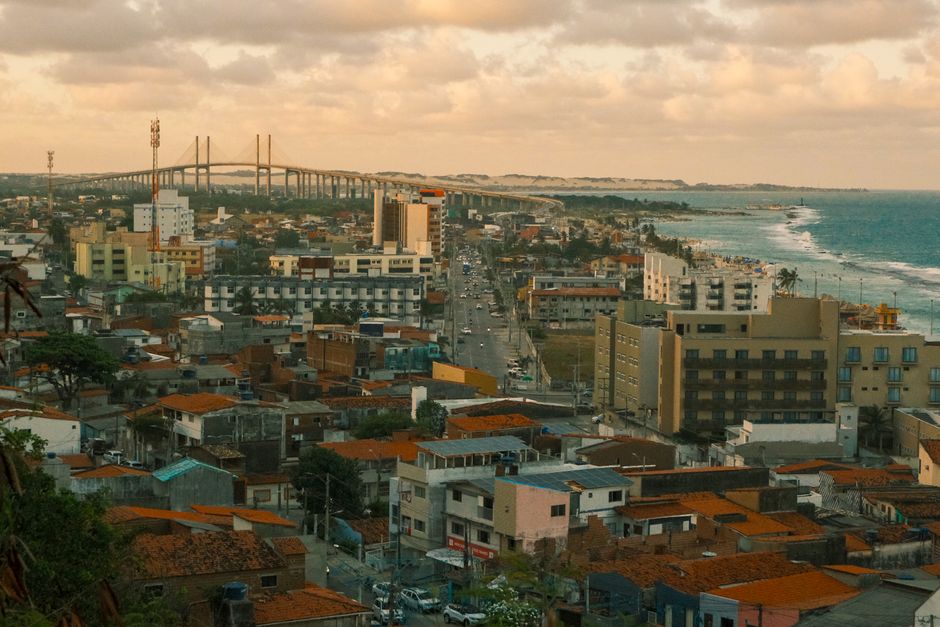 Scenic aerial view of Natal, Brazil, featuring cityscape and coastal bridge under a cloudy sky.